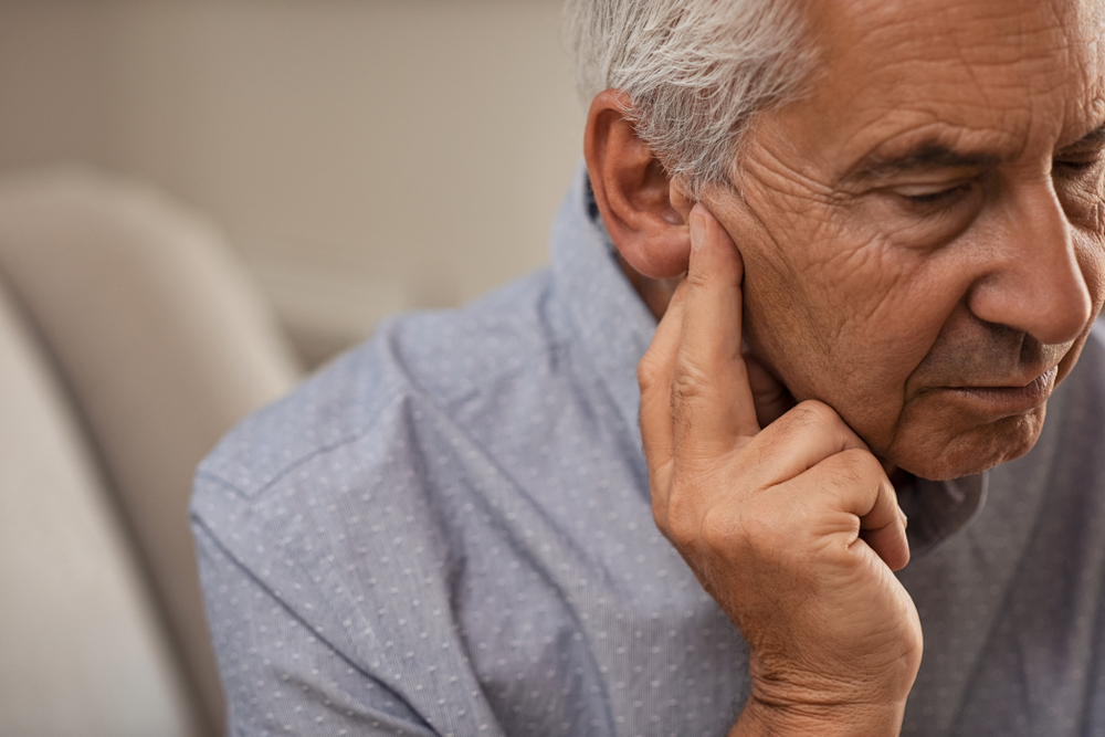 Mature man sitting on couch with fingers near ear.