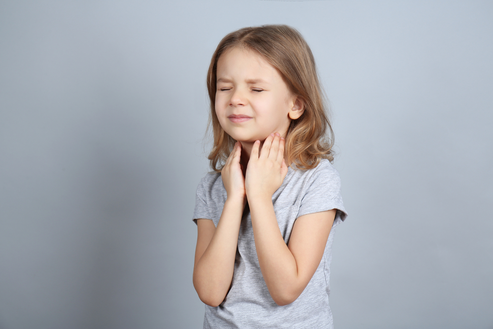 Girl with sore throat on grey background.