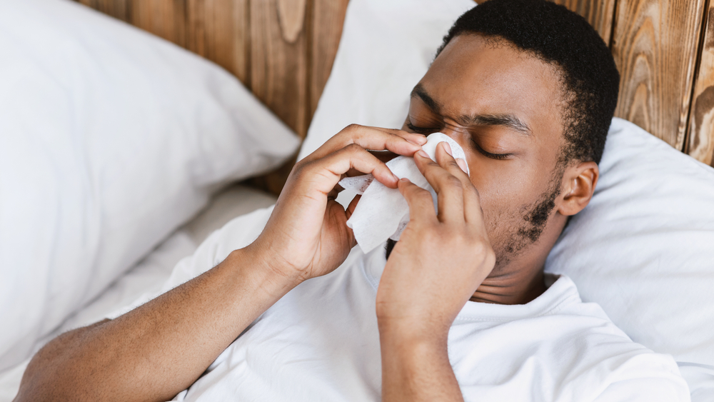 man suffering from sinus problems blowing nose in bed