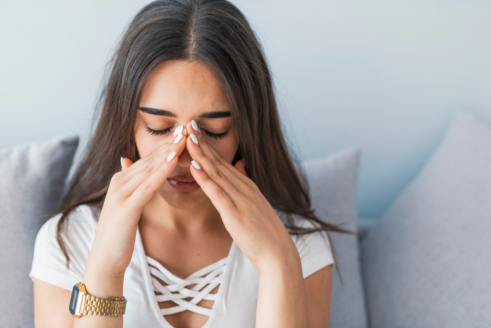 Sad woman holding her nose and head because sinus pain.